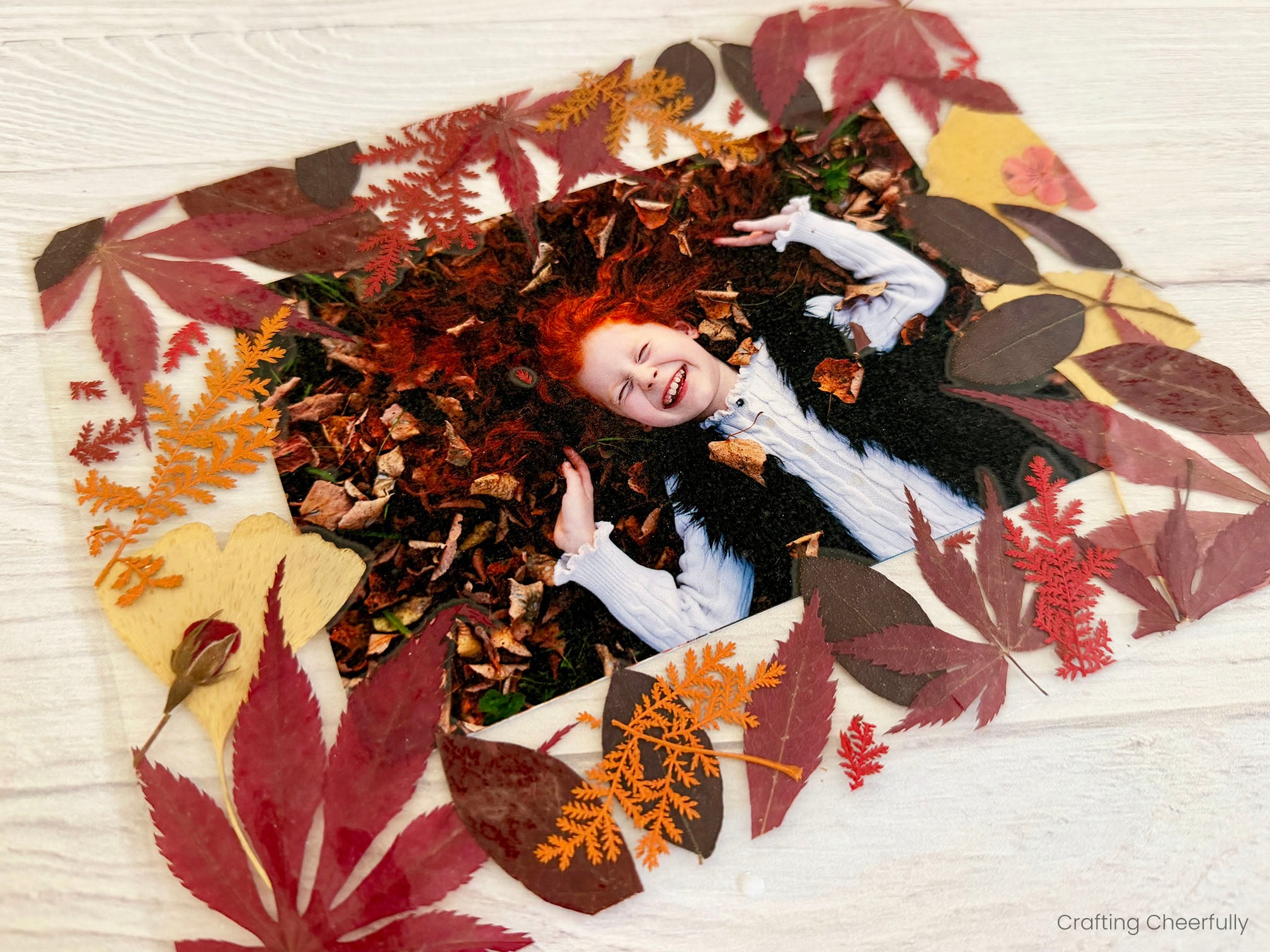 A photo of a little girl laying in leaves is shown in a frame made from pressed leaves.