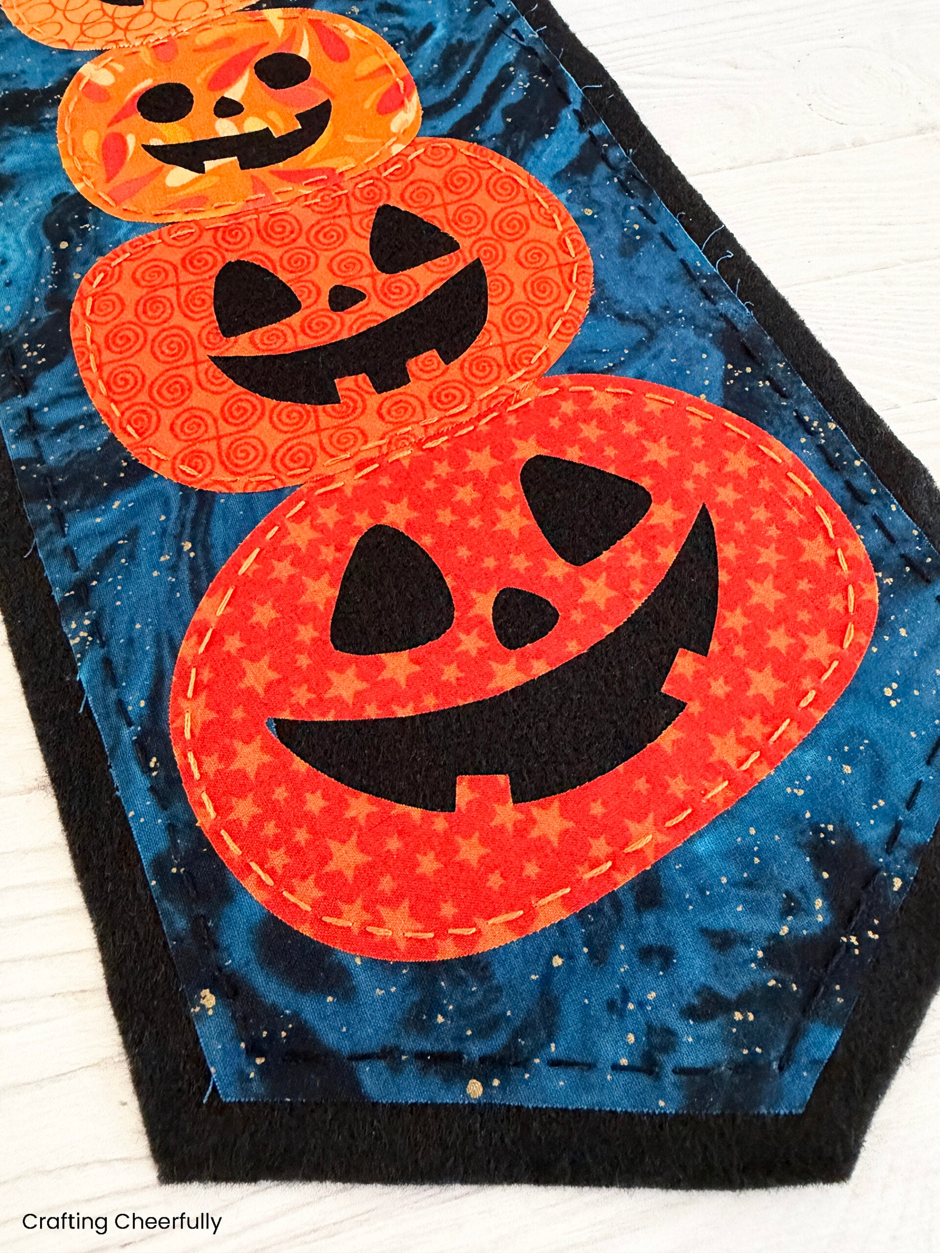 Fabric pumpkins stacked on top of each other with goofy jack-o'-lantern faces.
